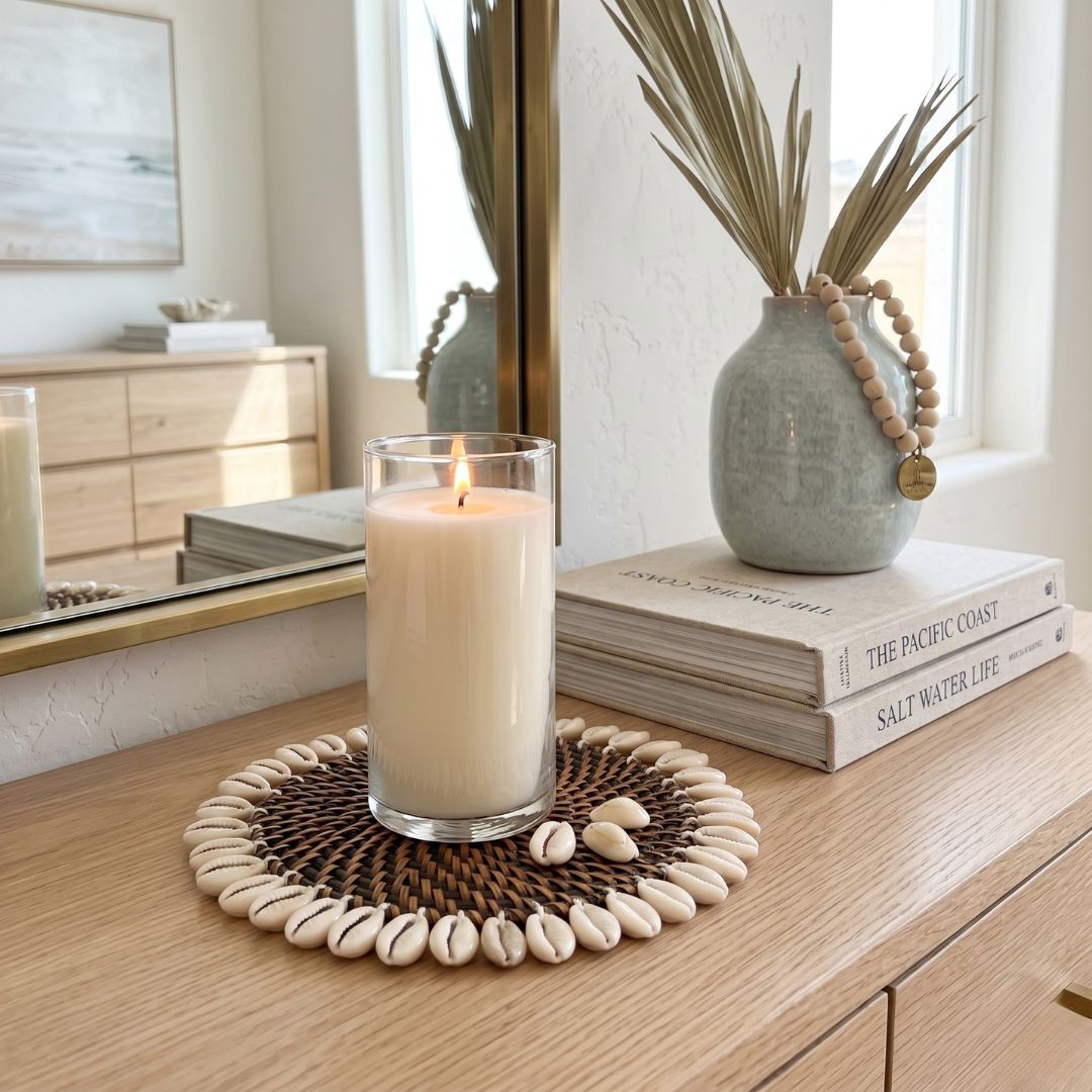 Candle on a woven coaster with a vase and books in the background
