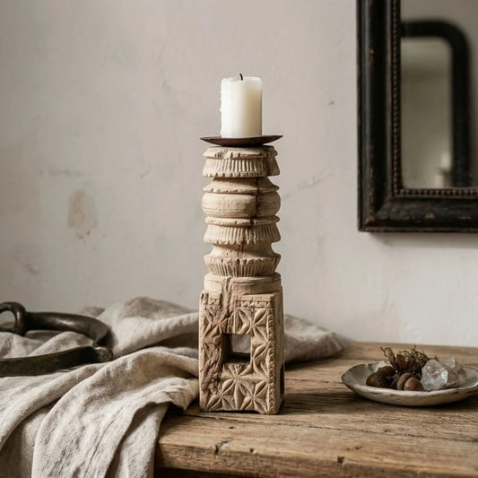 Decorative candle holder with a candle on a wooden surface, with a mirror and fabric in the background.