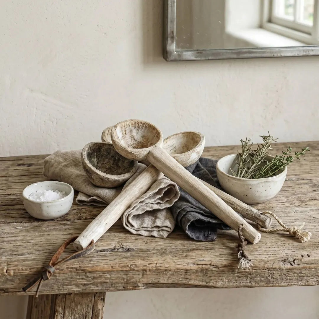 Set of rustic kitchen utensils including wooden ladle, bowls, and a towel on a wooden surface.