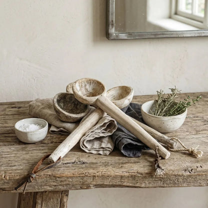 Set of rustic kitchen utensils including wooden ladle, bowls, and a towel on a wooden surface.