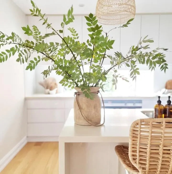 Vase with green leaves on a white table in a room with a window and decor.