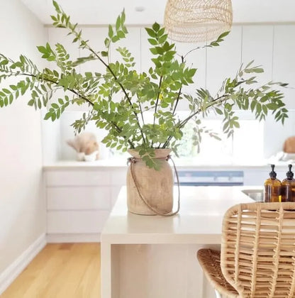 Vase with green leaves on a white table in a room with a window and decor.