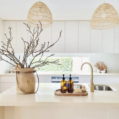 Modern kitchen with wicker pendant lights, a vase with branches, and a tray with bottles.