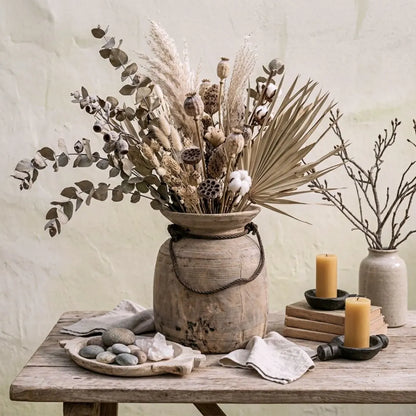 Vintage Indian Urn with decorative arrangement with dried plants in a rustic vase on a wooden table.