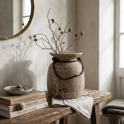 Wooden vase with dried branches on a wooden table with books and a mirror in the background