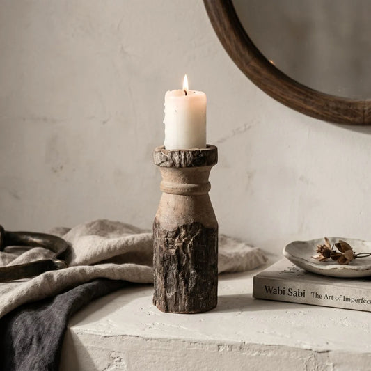 Candle in a rustic wooden holder on a surface with a book and decorative items.