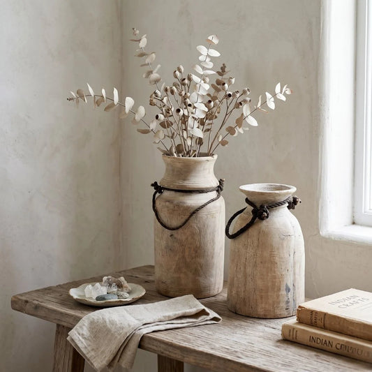 Two rustic vases with dried flowers on a wooden table in a softly lit room.
