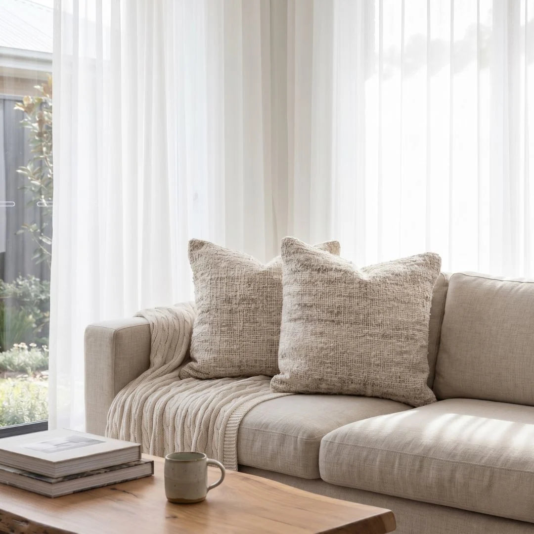 Beige sofa with textured cushions in a bright living room with large windows.