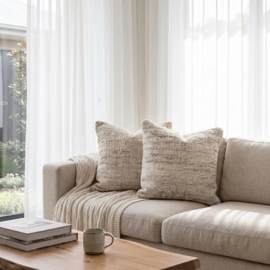 Beige sofa with textured cushions in a bright living room with large windows.