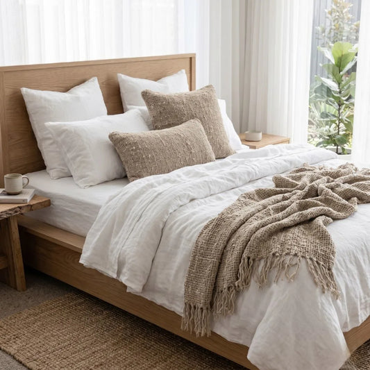Neatly made bed with white bedding and brown throw blanket in a bright bedroom.