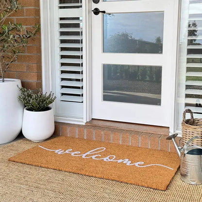 Welcome mat on a porch with plants and a door in the background