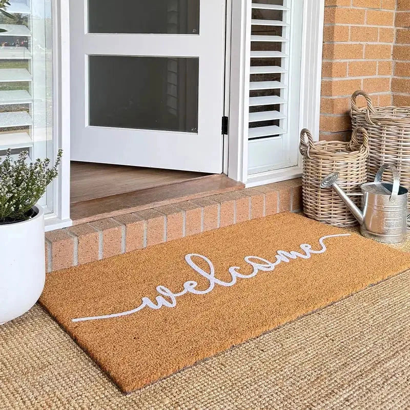 Coir doormat with 'welcome' text on a porch with a white door and brick wall.