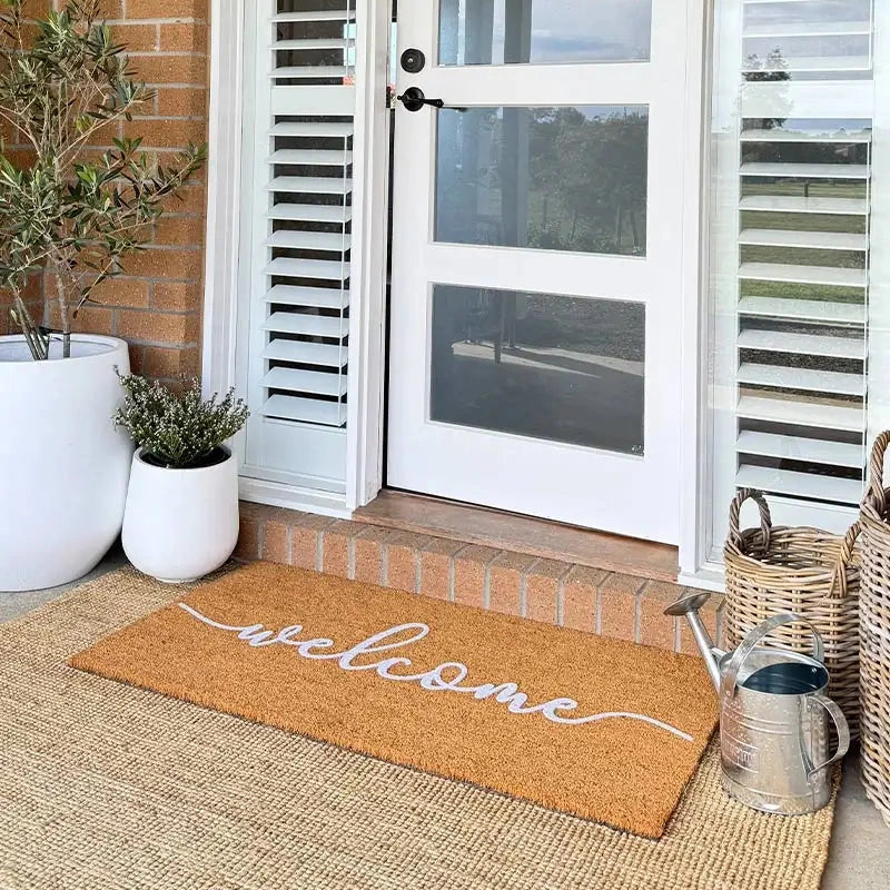 Front door with a 'welcome' mat, plants, and a basket on a brick porch.