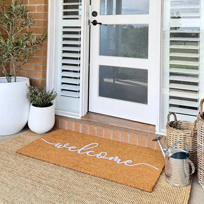 Front door with a 'welcome' mat, plants, and a basket on a brick porch.