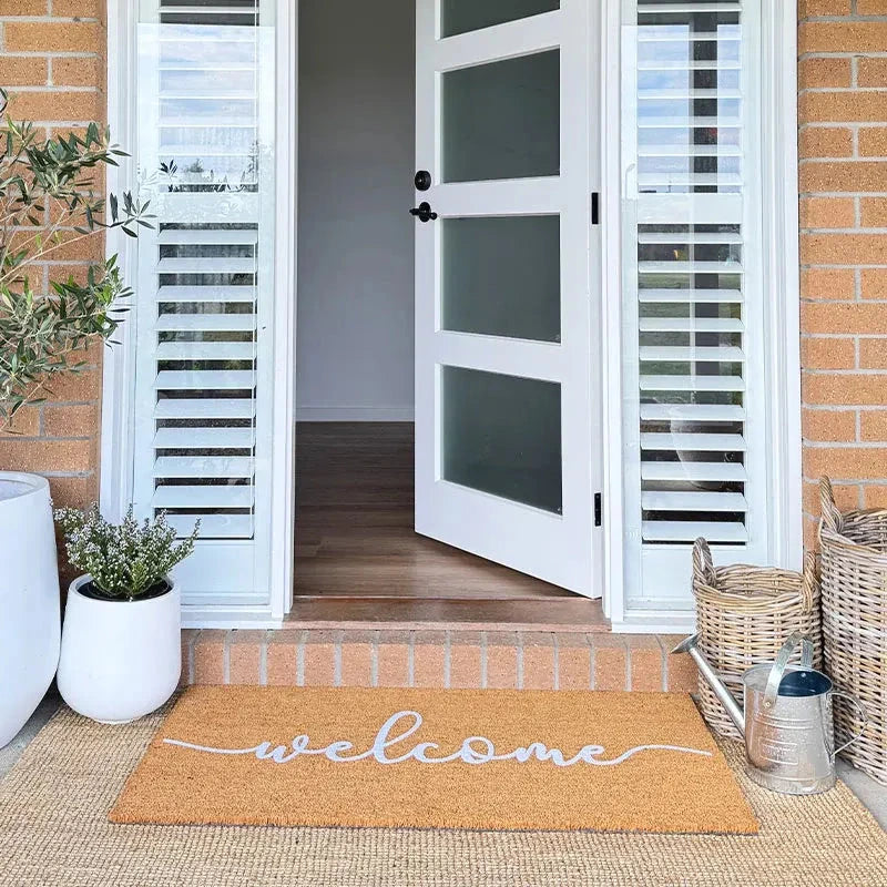 Open white door with glass panels on a brick wall, featuring a 'welcome' mat on the floor.