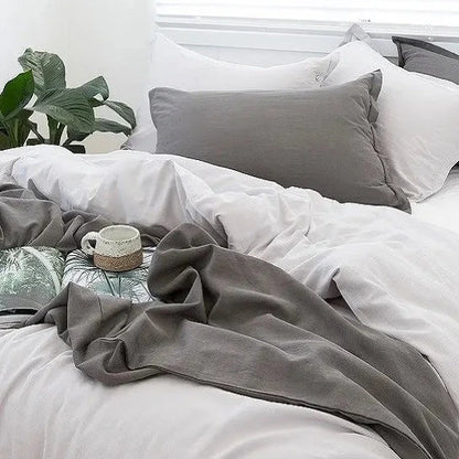 Neatly made bed with gray and white bedding, plant, and decor items.