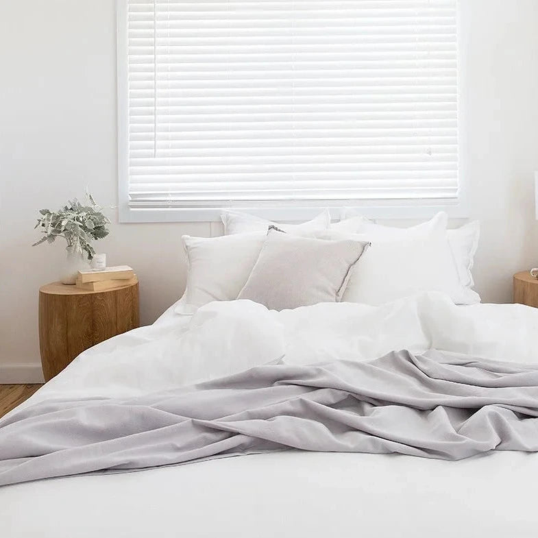 Neatly made bed with white bedding and gray blanket in a bedroom setting.