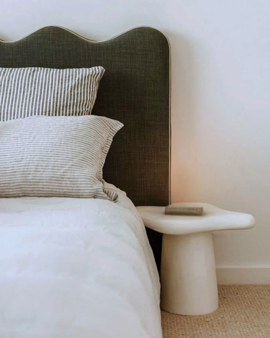 Bed with striped pillows and a textured headboard next to a white nightstand.