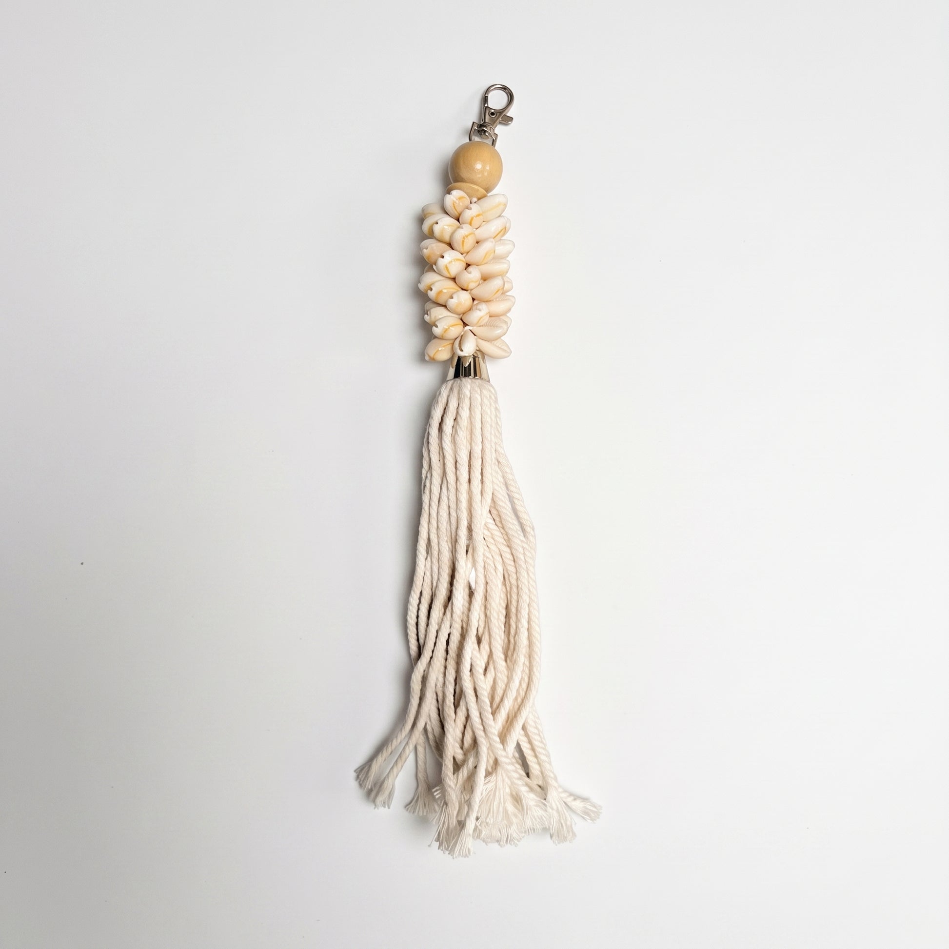 A bohemian-style tassel keychain featuring a light wood bead, a cluster of cream-colored seashells, and a long cream cotton tassel, shown on a plain white background.