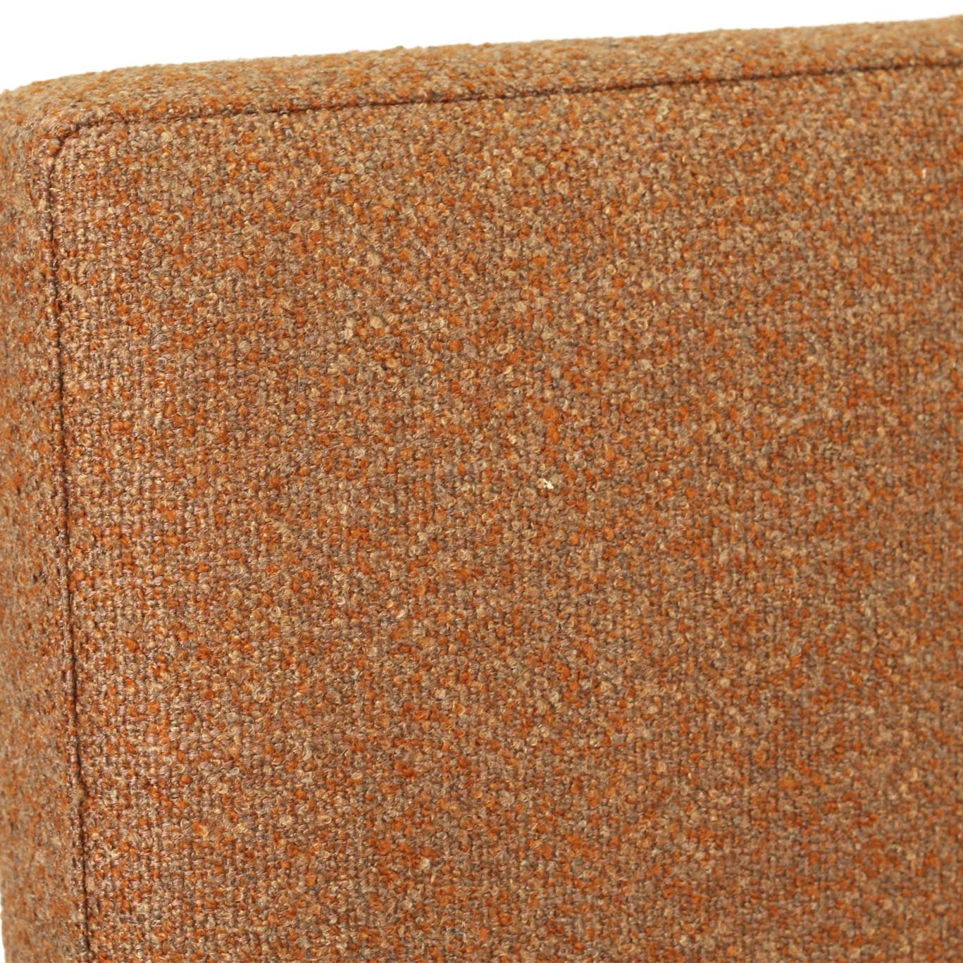 Close-up of a textured woven upholstery fabric in a warm rust-orange color, showing the weave detail and a vertical seam.