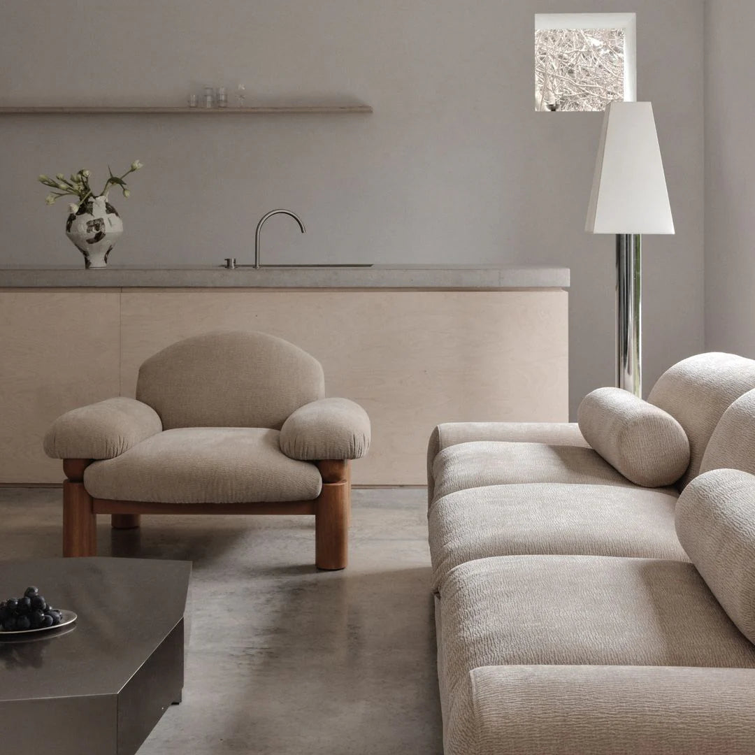 Modern living room with beige sofa and armchair, concrete floor, and minimal decor.