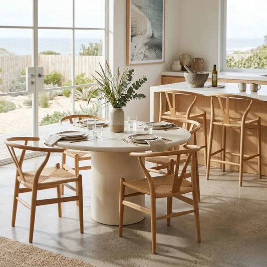 Dining area with a round table and wooden chairs in a bright room with large windows.