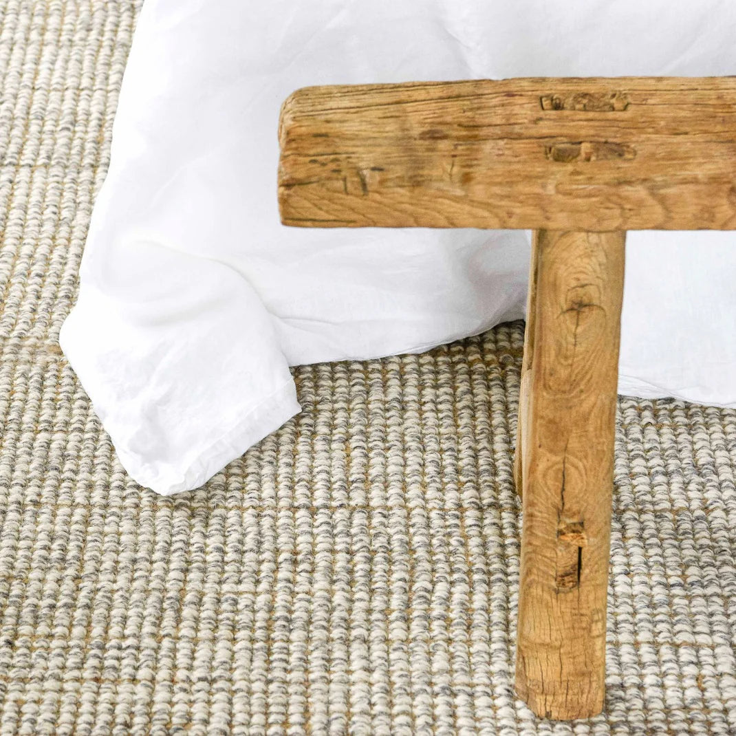 Wooden stool with a white cushion on a textured beige floor