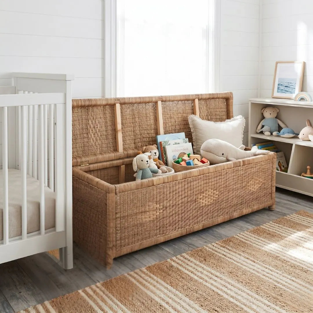 Wicker toy storage chest with children's toys in a room with a crib and bookshelf.