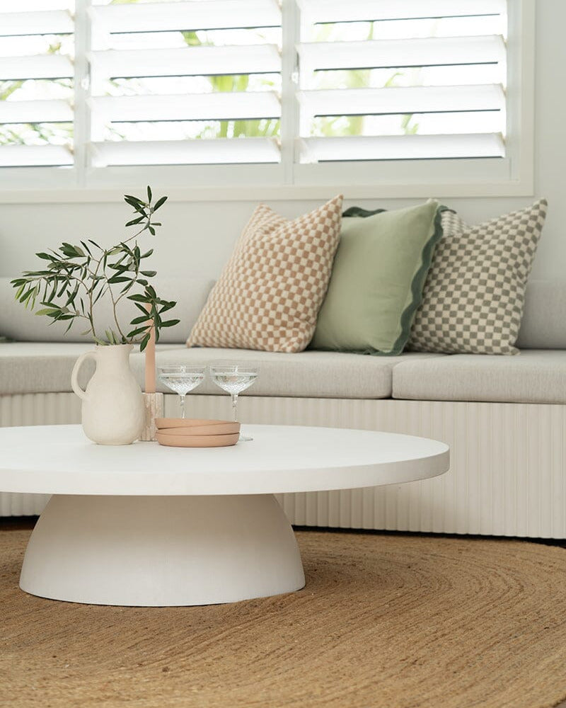 A white micro cement Xander Round Coffee Table placed in a living room setting, featuring a sleek, modern design with a smooth finish.