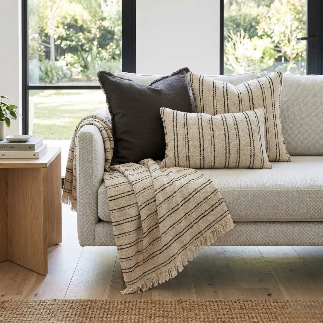 Beige sofa with striped cushions and a blanket in a bright living room.