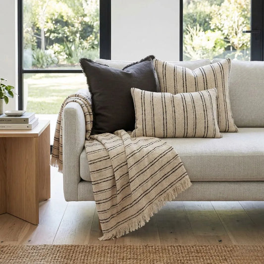 Beige sofa with striped cushions and a blanket in a bright living room.