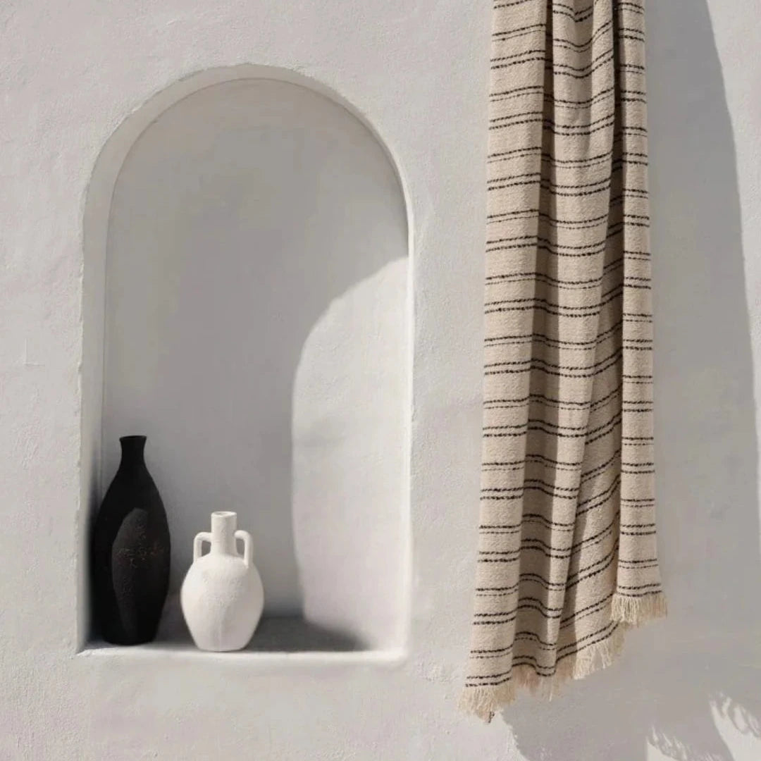 Striped towel hanging on a wall next to two vases in a niche.