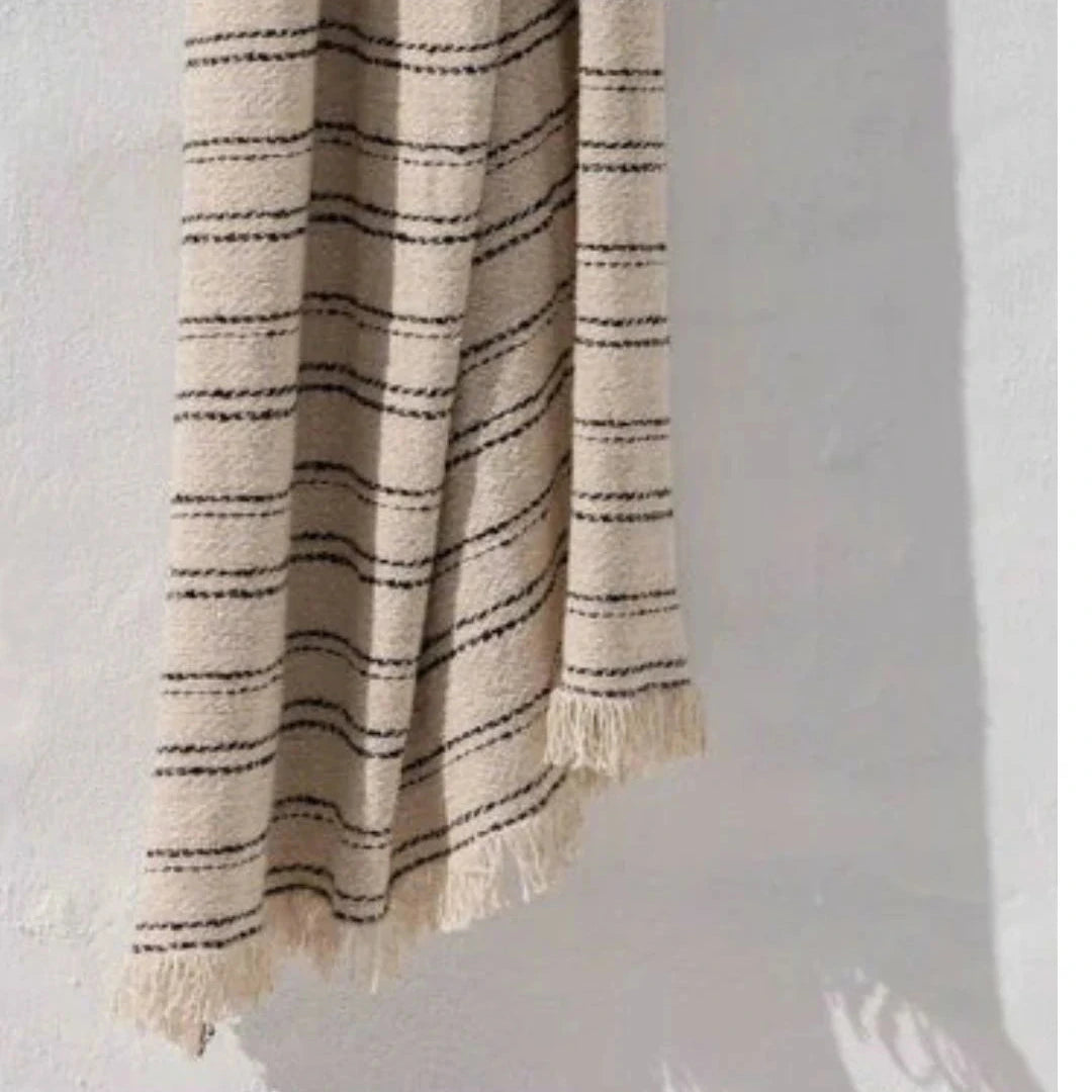 Beige and black striped blanket with tassels on a light gray background