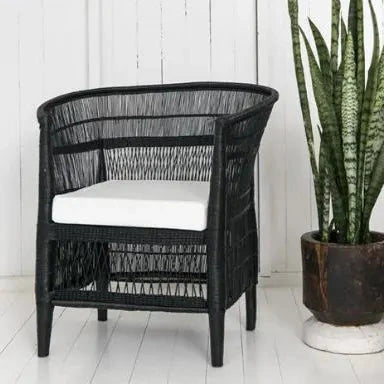 Black Malawi Cane chair with white cushion next to a potted plant on a white wooden floor.