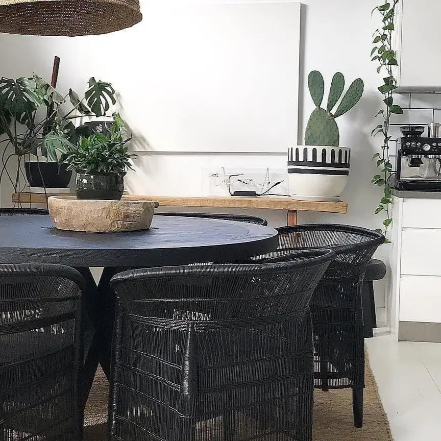 Dining area with black round table and chairs, plants, and a cactus wall art.