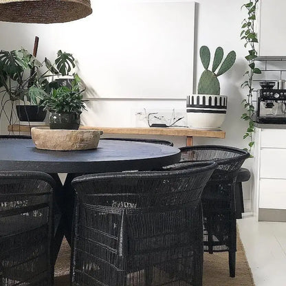 Dining area with black round table and chairs, plants, and a cactus wall art.