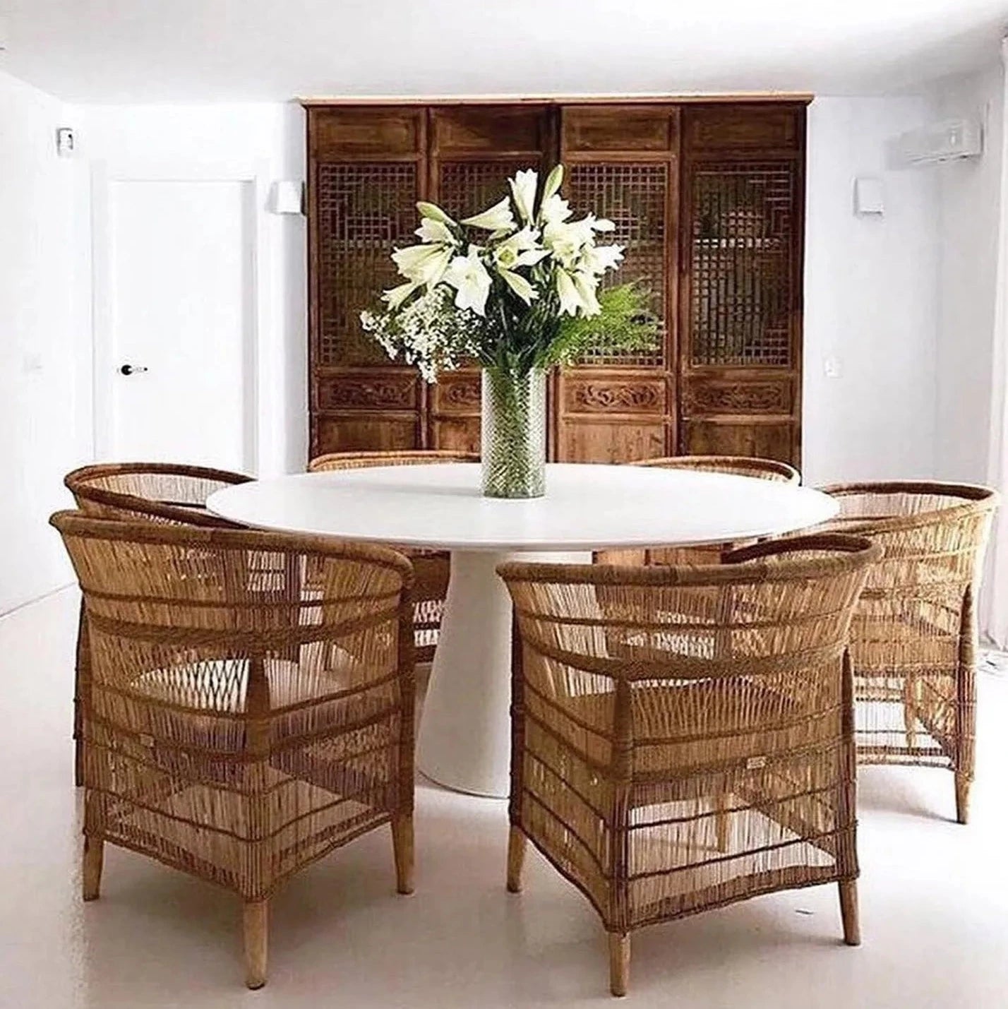 Dining area with wicker chairs around a round table, featuring a vase of flowers.