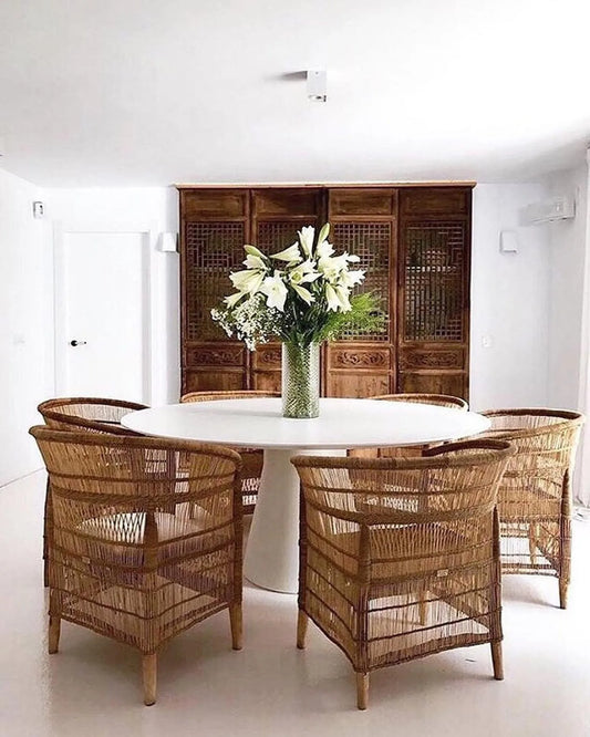 Dining area with wicker chairs around a round table, featuring a vase of flowers.
