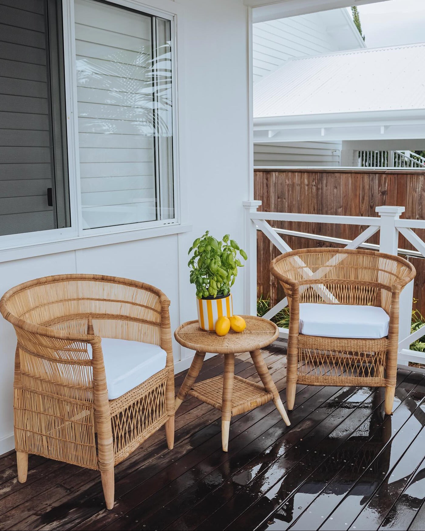 Two wicker chairs with white cushions and a small table on a wooden deck.