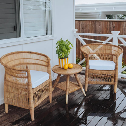 Two wicker chairs with white cushions and a small table on a wooden deck.