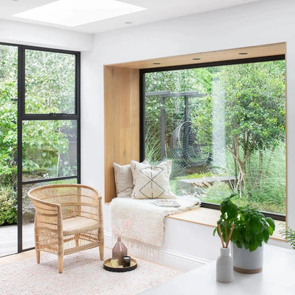 Modern living room with Sun Republics Malawi cane chair, sofa, and large windows overlooking greenery.