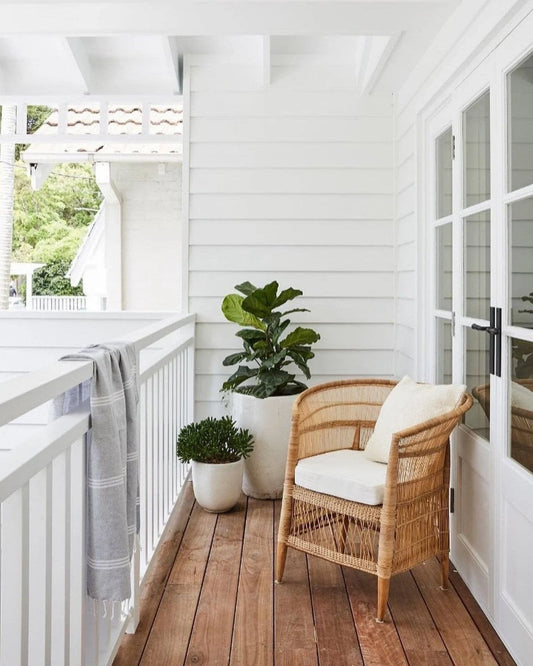 Balcony with wicker chair, potted plants, and white railing.