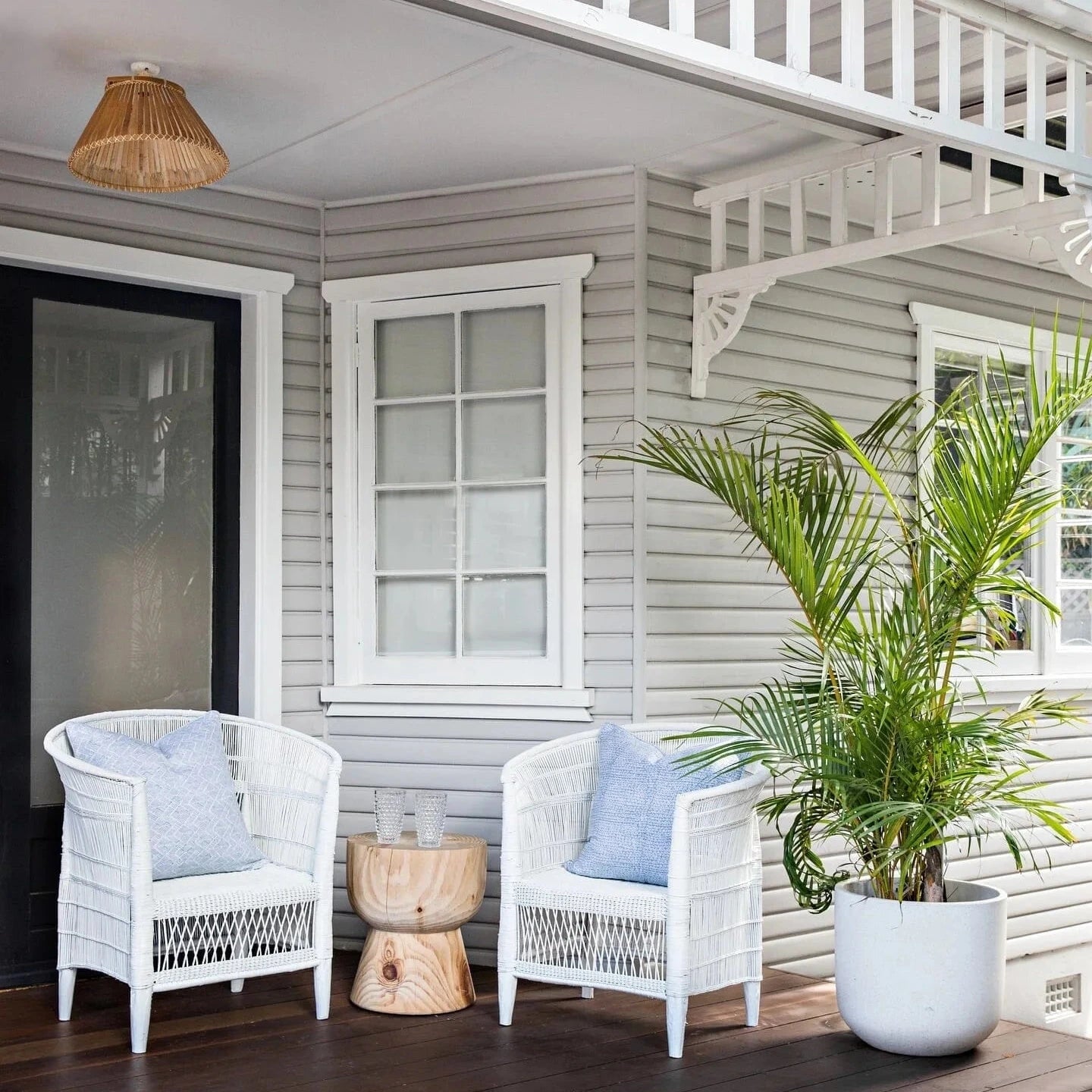 Two white wicker chairs with blue cushions on a wooden deck in front of a house.