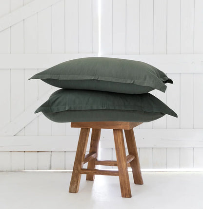 Two green pillows stacked on a wooden stool against a white paneled wall.