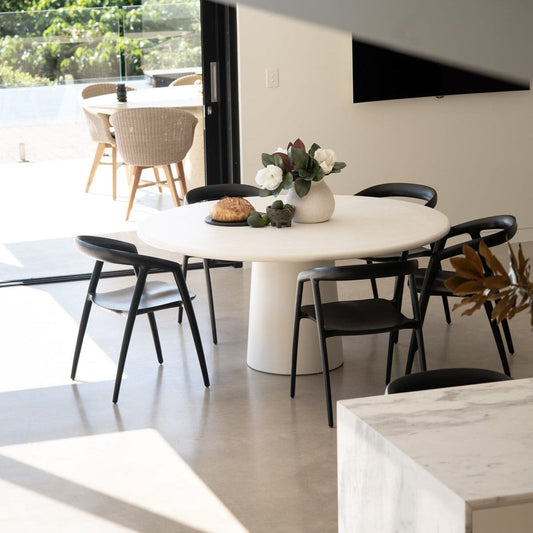 Modern dining area with a white round table and black chairs in a bright room.