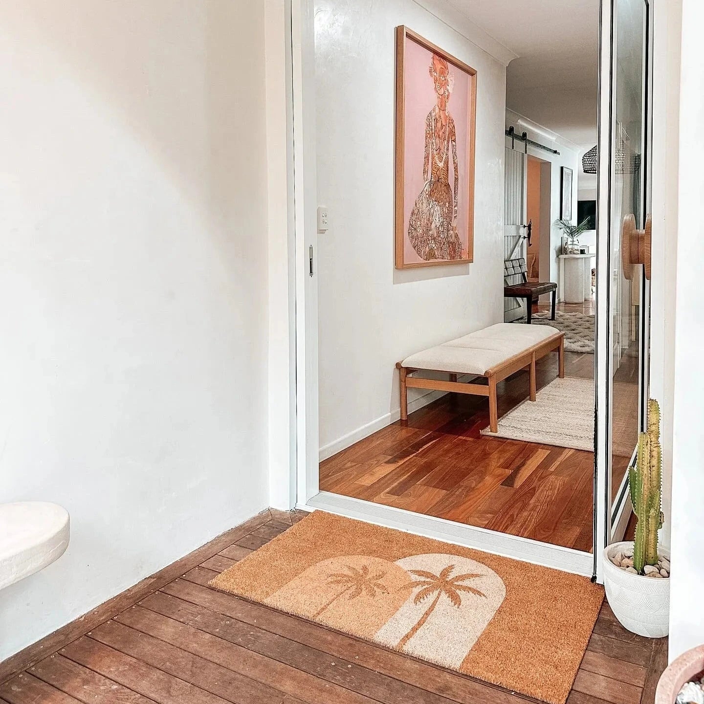 Entryway with wooden floor, doormat, and mirror reflecting interior.