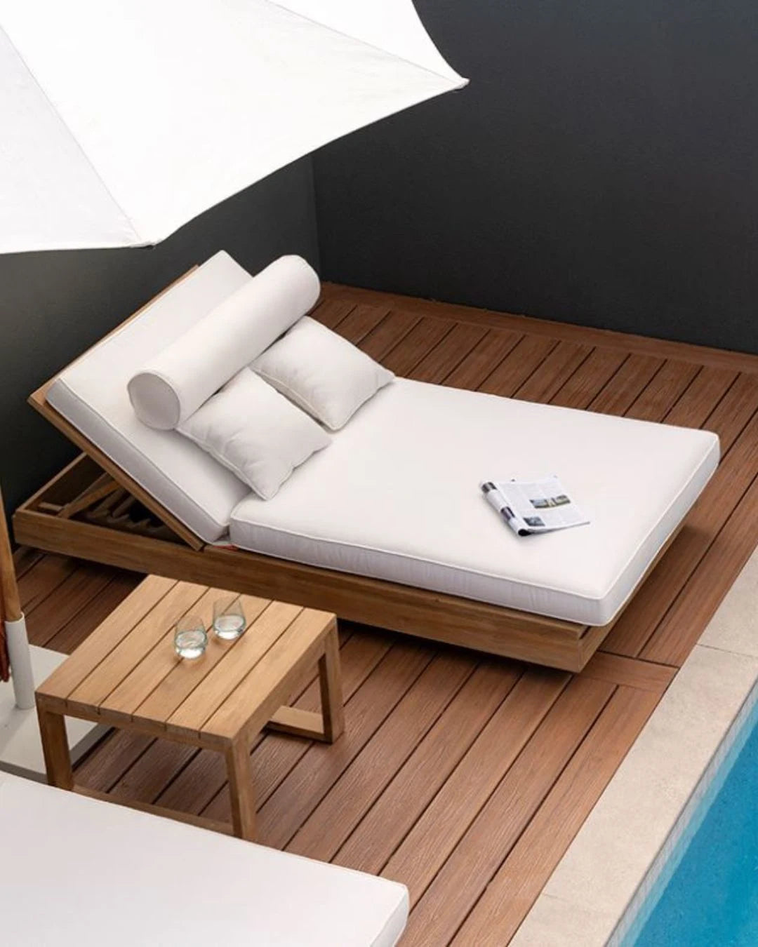Modern outdoor lounge chair with white cushions on a wooden deck by a pool.