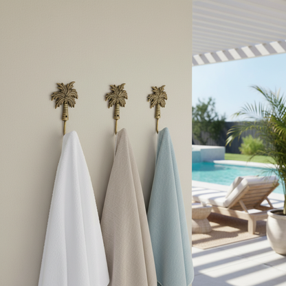 Three palm tree hooks with towels hanging on them, next to a pool area.