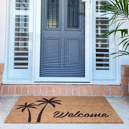 Doormat with palm tree design and 'Welcome' text in front of a glass door.