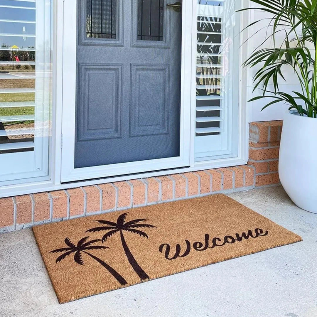 Coir doormat with palm tree design and 'Welcome' text on a porch with a blue door.